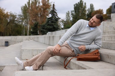 Photo of Man with injured leg on stairs outdoors after fall. Dangerous accident