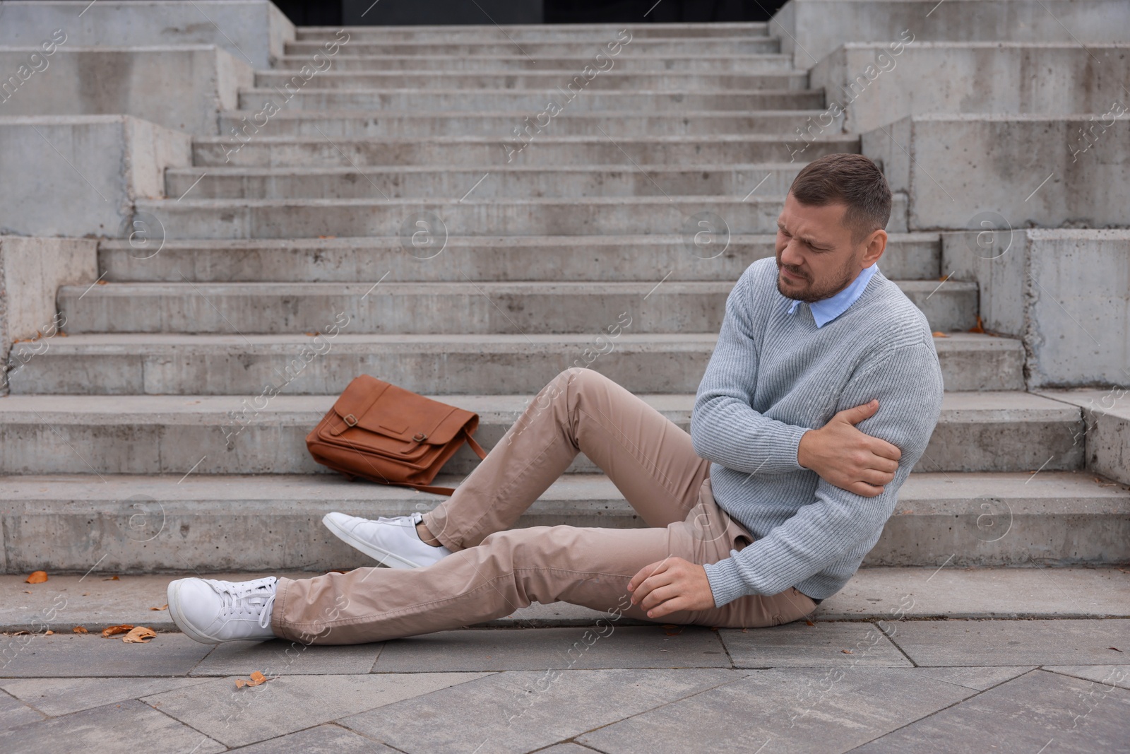 Photo of Man with injured arm on stairs outdoors after fall. Dangerous accident