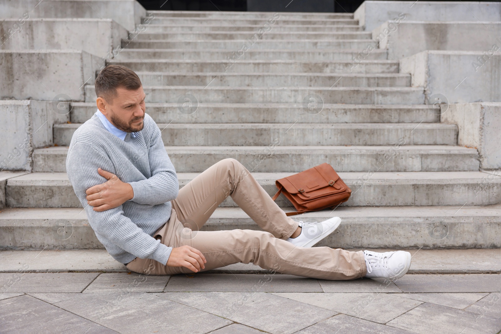 Photo of Man with injured arm on stairs outdoors after fall. Dangerous accident