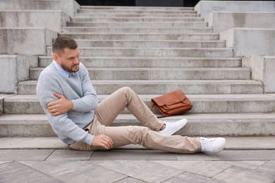 Photo of Man with injured arm on stairs outdoors after fall. Dangerous accident