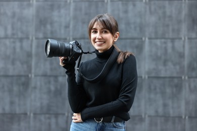 Photo of Professional photographer with digital camera near grey wall outdoors