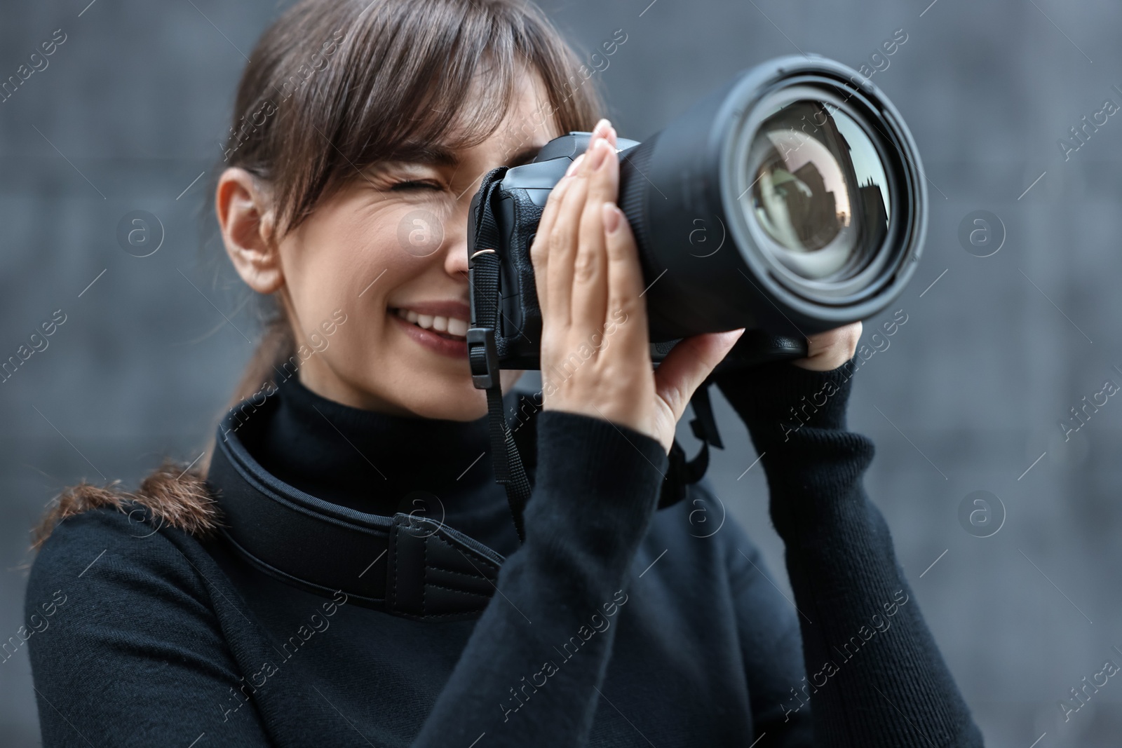 Photo of Professional photographer taking picture with camera near grey wall outdoors