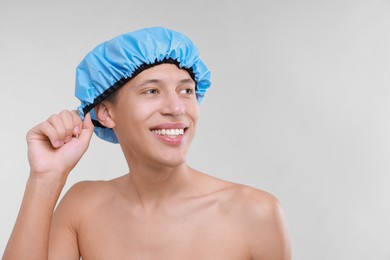 Photo of Happy man wearing shower cap on light grey background