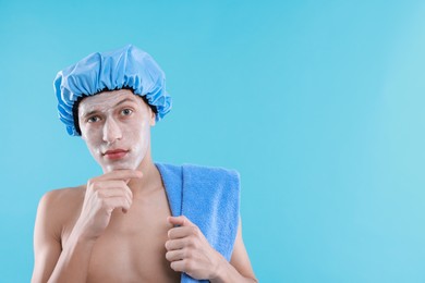 Man in shower cap with cream on his face against light blue background, space for text