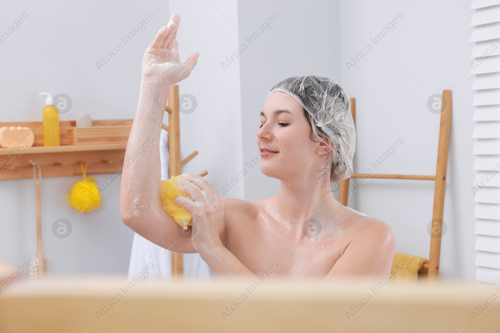 Photo of Woman with cap and mesh sponge taking shower in bathroom