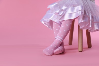 Photo of Child in tights sitting on stool against pink background, closeup. Space for text