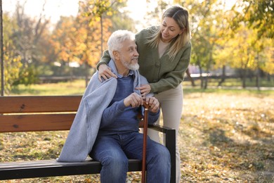 Caregiver assisting senior man on wooden bench in park. Home health care service