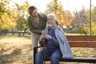 Photo of Caregiver assisting senior man on wooden bench in park. Home health care service