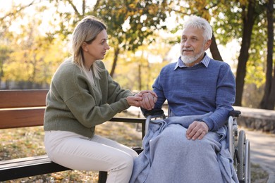 Photo of Caregiver assisting senior man on wheelchair in park. Home health care service