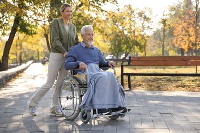 Caregiver assisting senior man on wheelchair in park, space for text. Home health care service