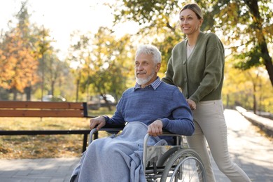 Photo of Caregiver assisting senior man on wheelchair in park. Home health care service