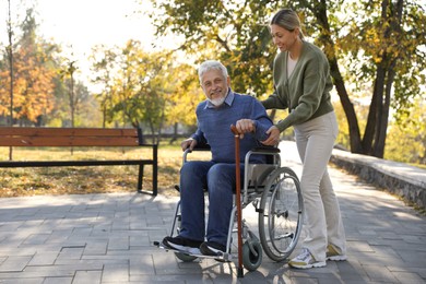 Photo of Caregiver assisting senior man on wheelchair in park, space for text. Home health care service