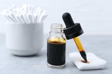 Photo of Bottle of iodine with dropper, piece of bandage and cotton swabs on grey table, closeup