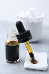 Photo of Bottle of iodine with dropper, piece of bandage and cotton swabs on grey table, closeup