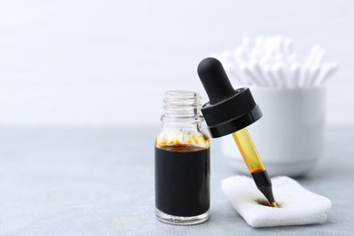 Photo of Bottle of iodine with dropper, piece of bandage and cotton swabs on grey table, closeup. Space for text