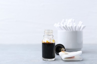 Photo of Bottle of iodine with dropper, piece of bandage and cotton swabs on grey table. Space for text