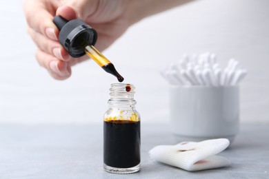 Photo of Woman taking iodine with dropper at grey table, closeup