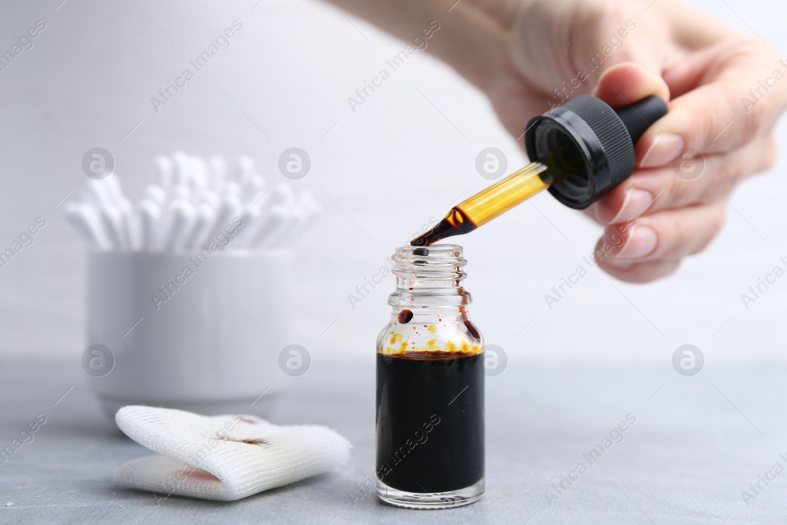 Photo of Woman taking iodine with dropper at grey table, closeup