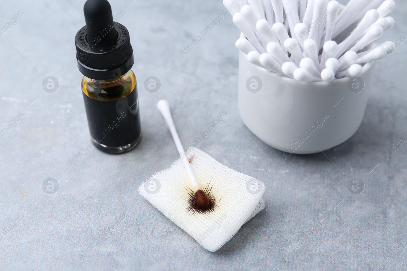 Photo of Bottle of iodine with dropper, piece of bandage and cotton swabs on grey table, closeup