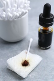 Photo of Bottle of iodine with dropper, piece of bandage and cotton swabs on grey table, closeup