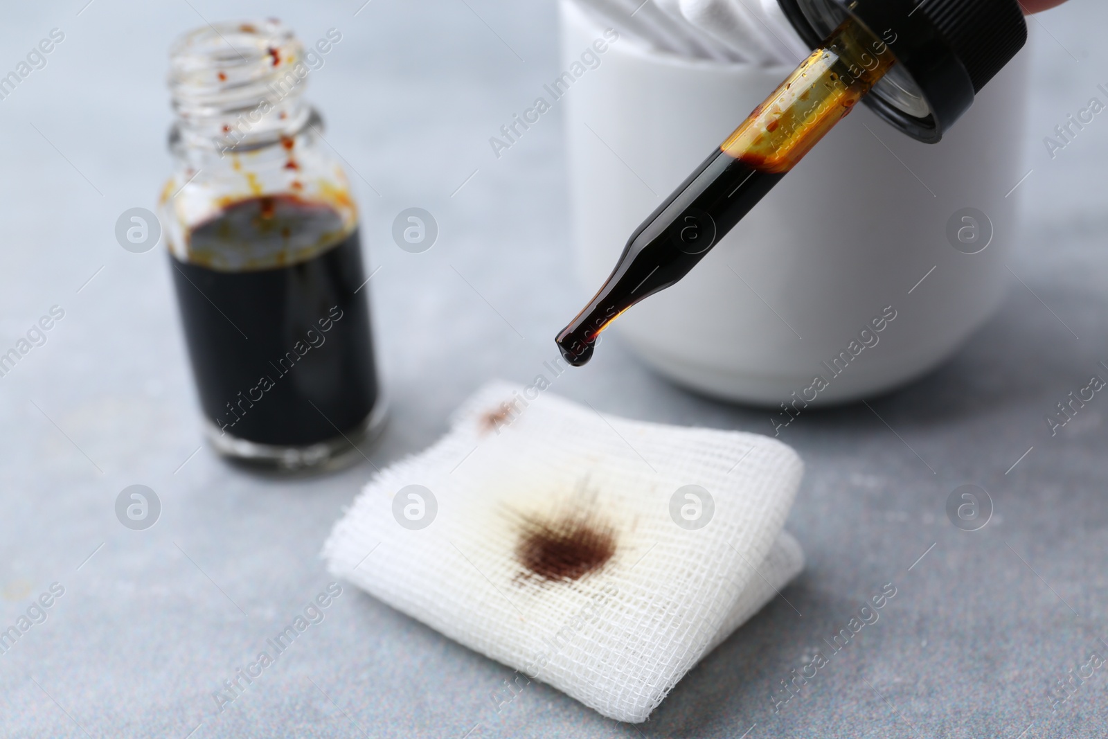 Photo of Dripping iodine on piece of bandage at grey table, closeup