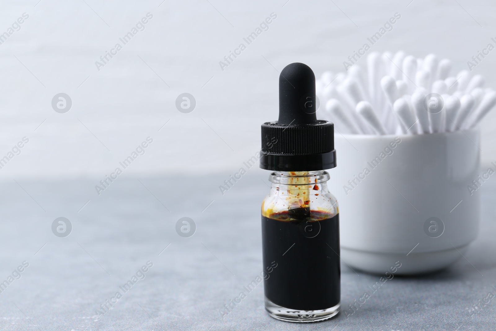 Photo of Bottle of iodine with dropper and cotton swabs on grey table, closeup. Space for text