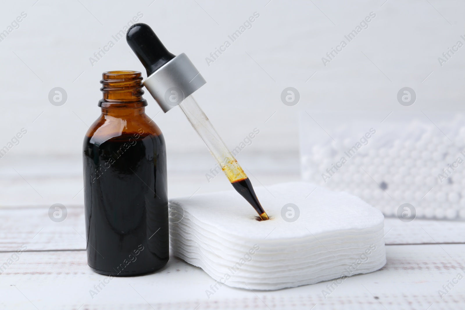 Photo of Bottle of iodine with dropper, cotton pads and swabs on white wooden table, closeup