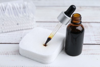 Photo of Bottle of iodine with dropper, cotton pads and swabs on white wooden table, closeup