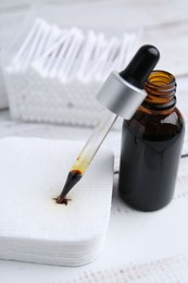 Photo of Bottle of iodine with dropper, cotton pads and swabs on white wooden table, closeup