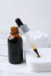 Photo of Bottle of iodine with dropper, cotton pads and swabs on white wooden table, closeup