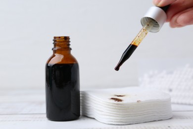 Photo of Woman dripping iodine on cotton pads at white wooden table, closeup