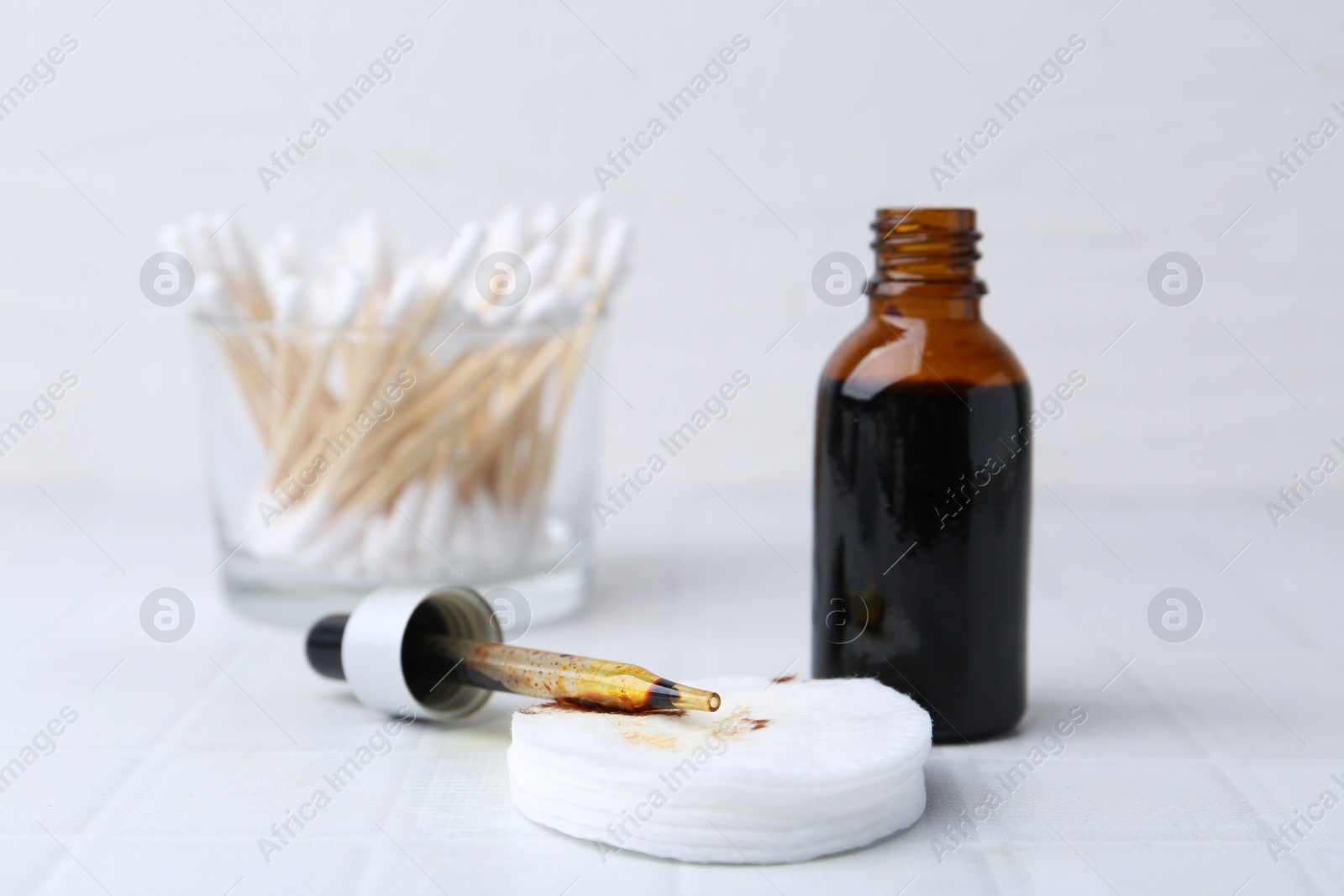 Photo of Bottle of iodine with dropper, cotton pads and swabs on white tiled table, closeup