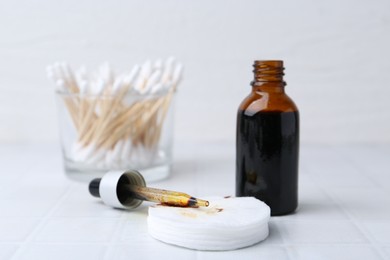 Photo of Bottle of iodine with dropper, cotton pads and swabs on white tiled table, closeup