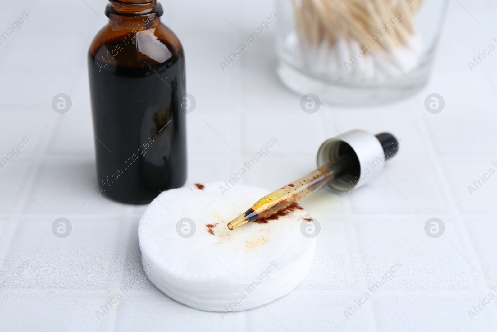 Photo of Bottle of iodine with dropper, cotton pads and swabs on white tiled table, closeup