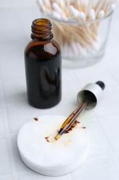 Photo of Bottle of iodine with dropper, cotton pads and swabs on white tiled table, closeup