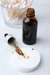 Photo of Bottle of iodine with dropper, cotton pads and swabs on white tiled table, closeup