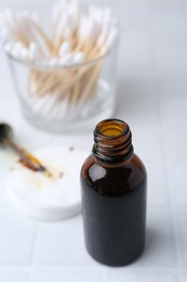 Photo of Bottle of iodine with dropper, cotton pads and swabs on white tiled table, closeup