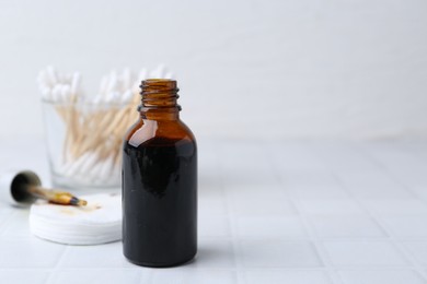 Photo of Bottle of iodine with dropper, cotton pads and swabs on white tiled table, closeup. Space for text