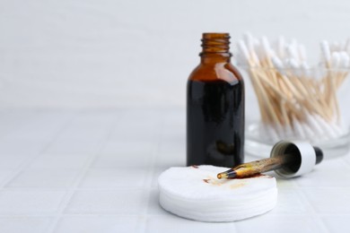 Photo of Bottle of iodine with dropper, cotton pads and swabs on white tiled table, closeup. Space for text