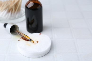 Photo of Bottle of iodine with dropper, cotton pads and swabs on white tiled table, closeup. Space for text