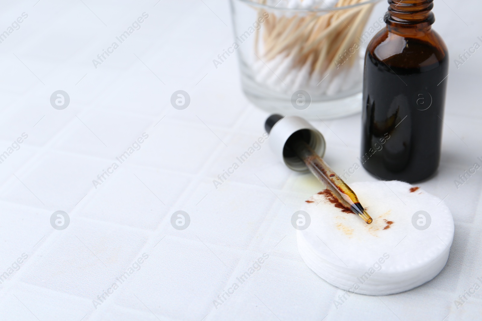 Photo of Bottle of iodine with dropper, cotton pads and swabs on white tiled table, closeup. Space for text