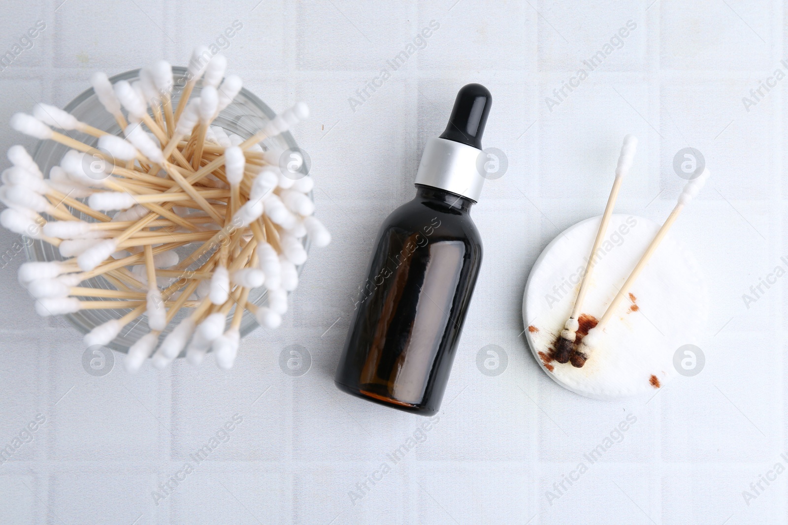 Photo of Bottle of iodine with dropper, cotton pads and swabs on white tiled table, flat lay