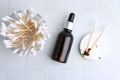 Photo of Bottle of iodine with dropper, cotton pads and swabs on white tiled table, flat lay