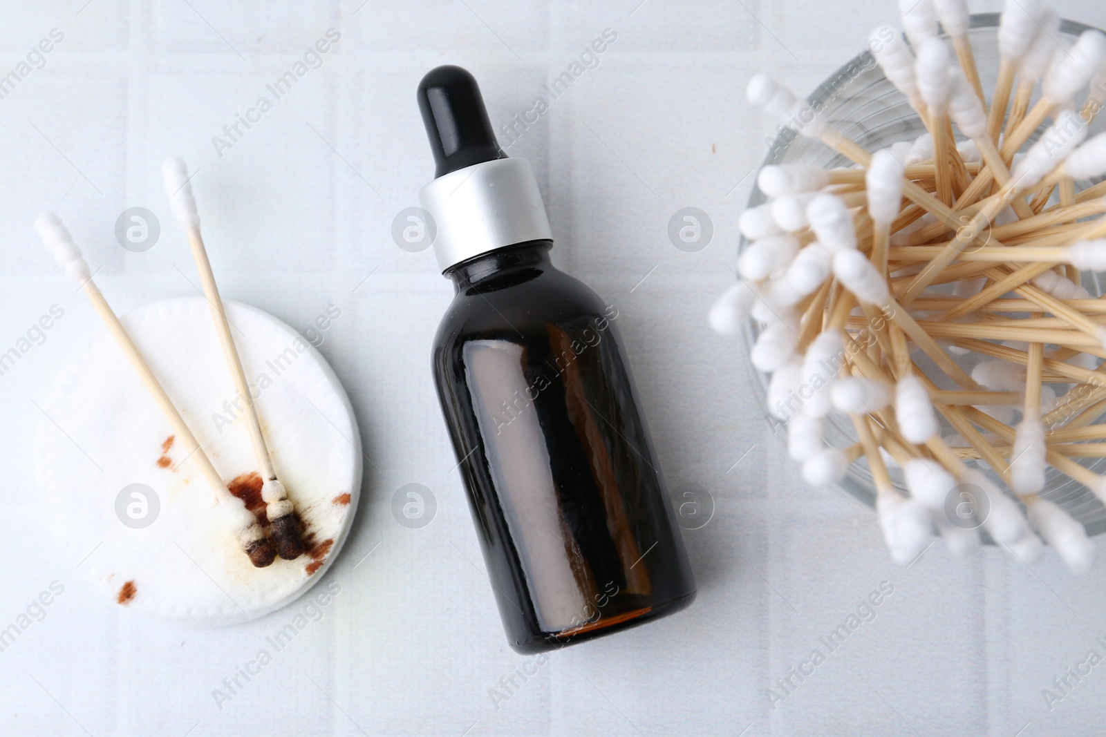 Photo of Bottle of iodine with dropper, cotton pads and swabs on white tiled table, flat lay