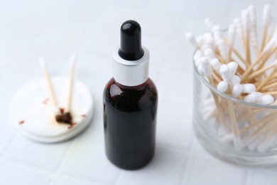 Photo of Bottle of iodine with dropper, cotton pads and swabs on white tiled table, closeup