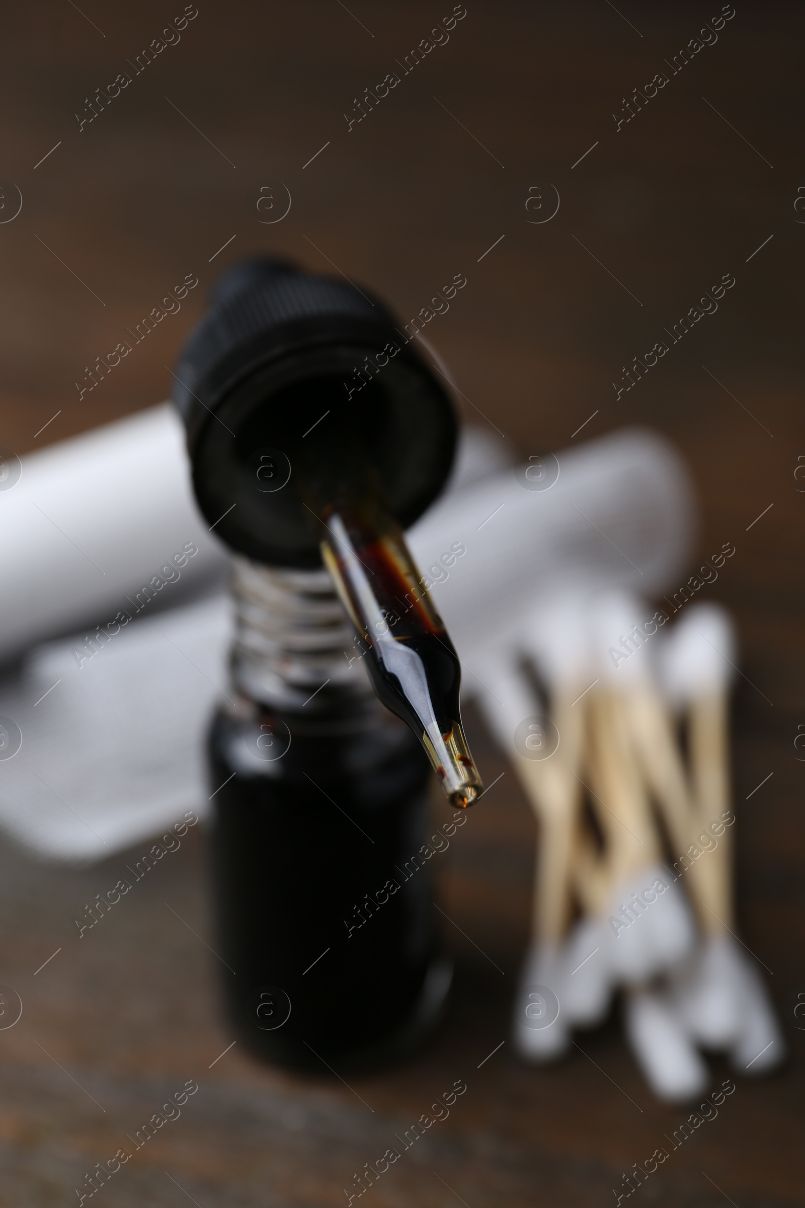 Photo of Bottle of iodine with dropper, cotton swabs and bandage on wooden table, closeup