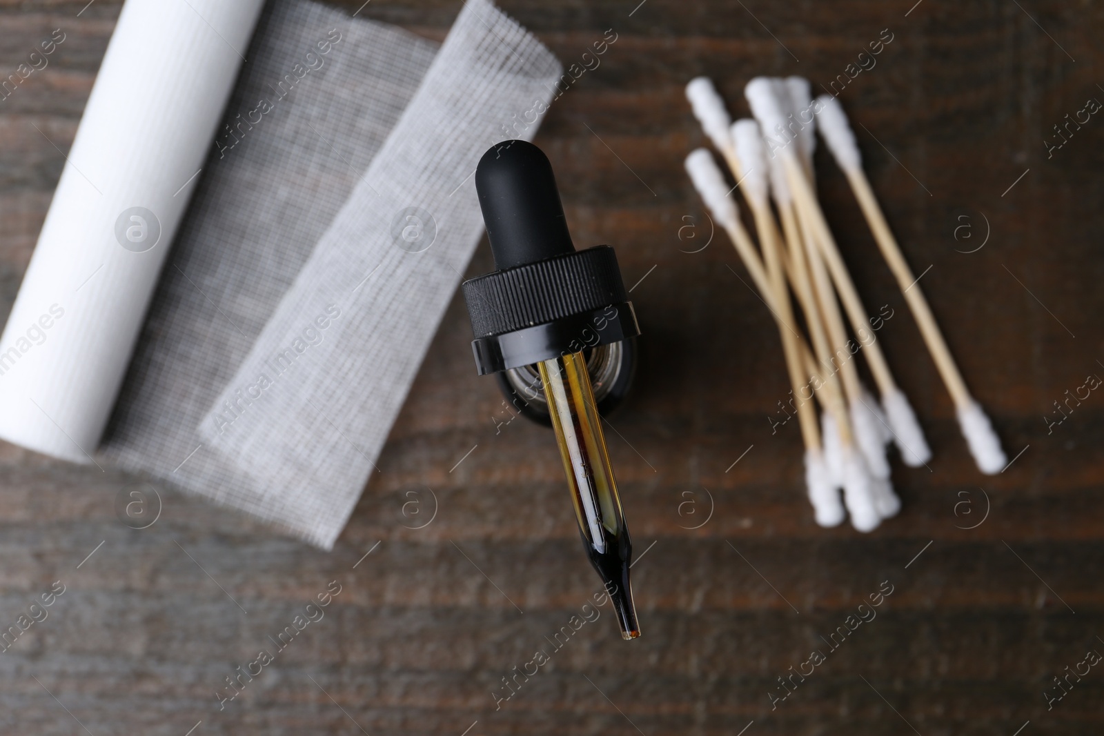 Photo of Bottle of iodine with dropper, cotton swabs and bandage on wooden table, flat lay