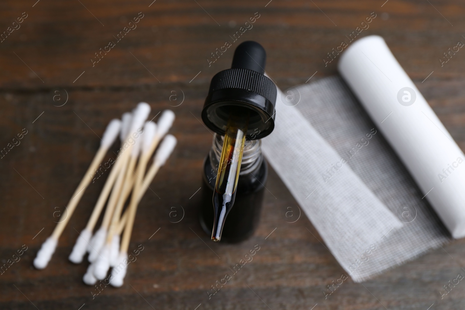 Photo of Bottle of iodine with dropper, cotton swabs and bandage on wooden table, closeup