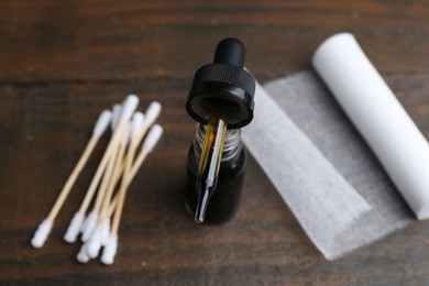 Photo of Bottle of iodine with dropper, cotton swabs and bandage on wooden table, closeup