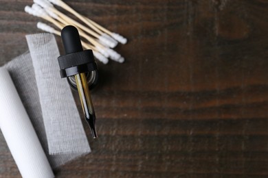 Photo of Bottle of iodine with dropper, cotton swabs and bandage on wooden table, flat lay. Space for text